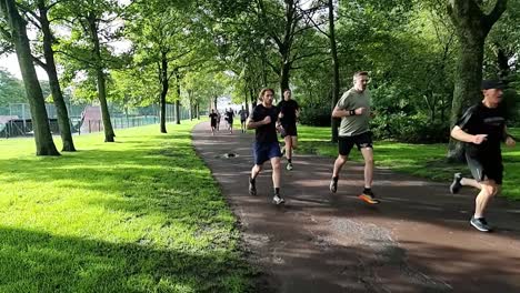 Slow-motion-group-of-people-running-together-in-charity-endurance-marathon-in-shaded-public-park