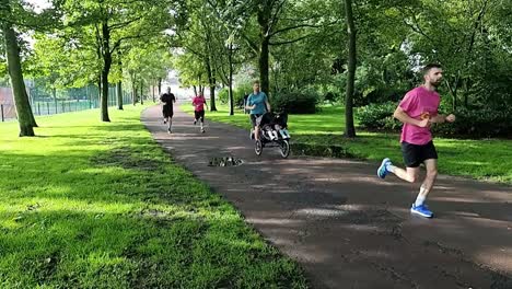 Slow-motion-young-adult-father-pushing-infants-running-in-charity-marathon-in-shaded-public-park