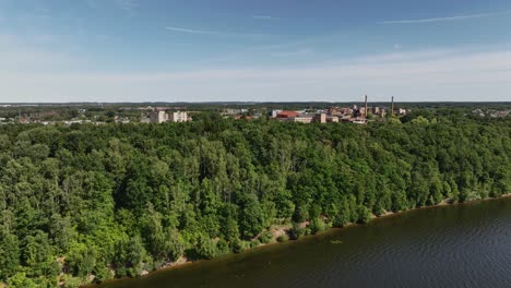 Aerial-view-The-shore-of-the-lake-is-covered-with-trees,-and-behind-them-you-can-see-the-buildings-of-the-town
