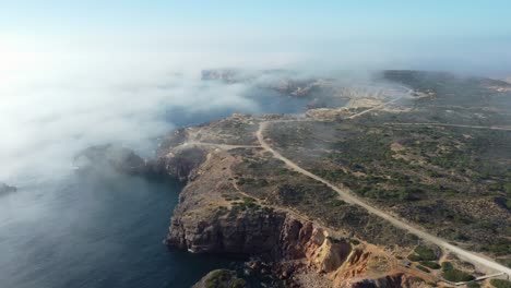 Aerial-pullback-of-scenic-Rocky-coastline-shrouded-in-fog,-Portugal-Southeast