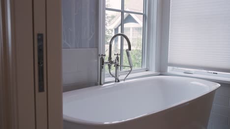 Closeup-of-white-bathtub,-silver-spout,-and-blue-wallpaper