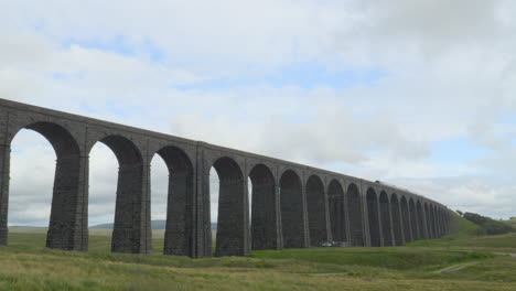 Viaduct-bridge-over-moorland-on-windy-overcast-summer-afternoon-with-passing-train-at-Ribblehead-Viaduct,-Yorkshire,-UK