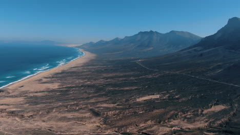 Cofete-beach,-Fuerteventura:-aerial-view-traveling-in-towards-a-fantastic-beach-and-the-great-mountains-that-surround-it
