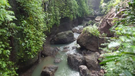 Arroyo-De-Río-En-Un-Arroyo-Cubierto-De-Musgo-Formado-Por-Agua-Que-Fluye-Desde-La-Cascada-De-Suwat-Corriendo-A-Través-De-Un-Cañón-De-Selva-Rocosa-De-Barro-En-Bali,-Indonesia