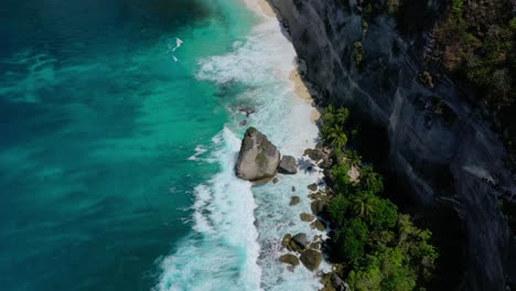 Unlock-the-magic-of-Bali's-Diamond-Beach-with-our-aerial-footage,-Discover-Diamond-Beach-With-its-ivory-sands,-crystalline-waters,-iconic-rock-formations,-and-true-tropical-paradise