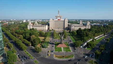 Vista-Aérea-De-La-Casa-Del-Edificio-De-Prensa-Libre-En-Bucarest,-Rumania,-Pasando-Por-Un-Alto-Edificio-De-Oficinas,-Rodeado-De-Vegetación-Verde.