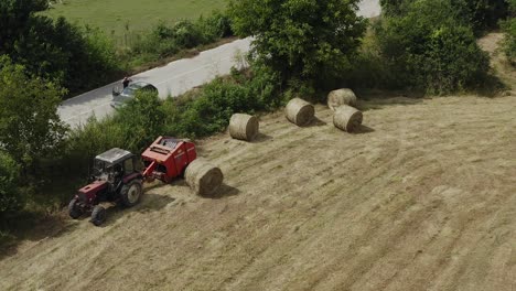 Drone-shot-above-bales-of-hay-in-field-with-tractor-and-farm-machinery