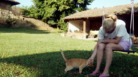 Amante-De-Los-Gatos-Sentado-En-El-Columpio-Del-Jardín,-Caricias-Y-Abrazos,-Linda-Mascota,-Gato-Pelirrojo