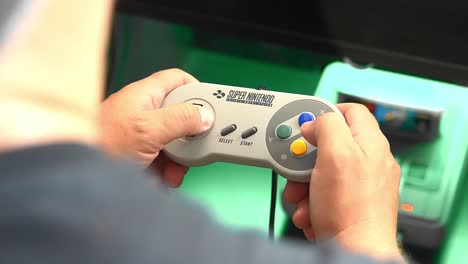 Gamer's-hand-maneuvers-and-play-super-nintendo-controller,-over-the-shoulder-handheld-close-up-shot
