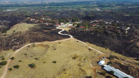 Slow-aerial-pull-back-over-a-village-surrounded-by-burned-land-in-the-aftermath-of-a-wildfire-in-northern-Greece,-August-2023