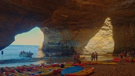 People-Gathering-Near-Kayaks-Under-Magnificent-Cave-On-Sandy-Beach,-Benagil,-Portugal