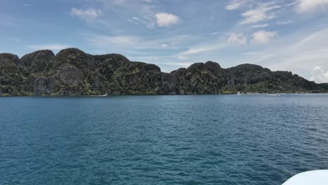 Isla-Tropical-Koh-Phi-Phi-Con-Un-Viaje-En-Ferry-Y-Bandera-Tailandesa-Ondeando-En-El-Viento-Acercándose-A-Tierra,-Tailandia