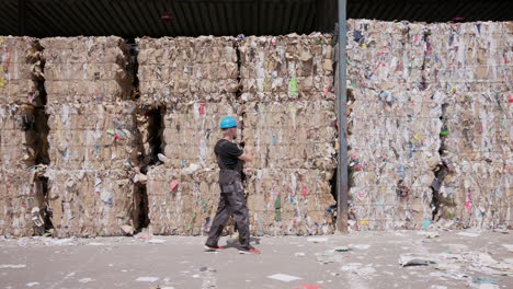 Wide-tracking-shot-of-worker-counting-paper-bales-at-recycling-plant