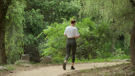 Young-Sporty-Woman-in-Sport-Clothes-Walking-in-a-Park-Doing-Morning-Cardio---Slow-motion-Back-view