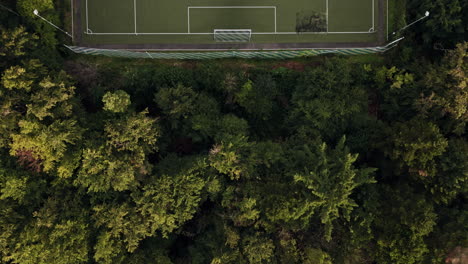 Aerial-top-down-view-of-green-football-field-in-the-middle-of-the-forest,-Drone-Fly-Over,-with-sun-and-shadows