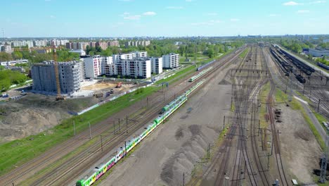 Scenic-Aerial-Shot-of-Passenger-Train-driving-into-Sunset-on-Train-Tracks-surrounded-by-Trees-above-Cityscape-forward