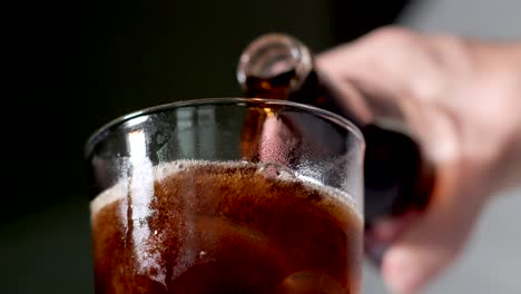 Hand-Pouring-Coke-or-Cola-From-a-Glass-Bottle-Into-Icy-Transparent-Drinking-Glass-Outdoors---Closeup-Low-Angle-View