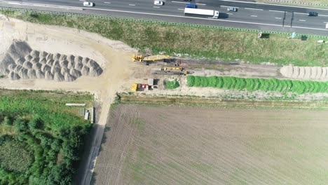 Very-high-aerial-drone-shot-of-a-construction-site-next-to-a-highway