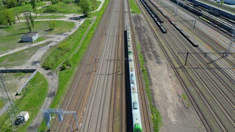 Szenische-Luftaufnahme-Eines-Personenzuges,-Der-Auf-Von-Bäumen-Umgebenen-Bahngleisen-über-Dem-Stadtbild-Vorwärts-In-Den-Sonnenuntergang-Fährt