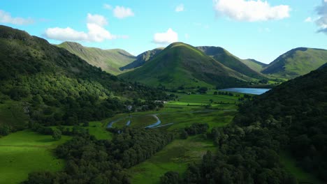 Lush-green-valley-surrounded-by-wooded-mountains-with-small-lake-Brotherswater-on-summer-day