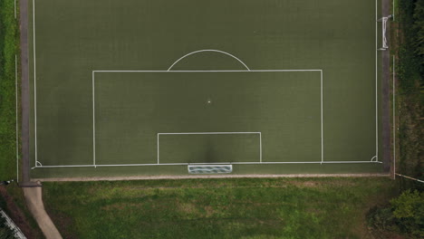 Top-Down-View-of-a-football-goal-on-an-empty,-green-football-field-in-the-middle-of-the-forest,-Drone-Footage