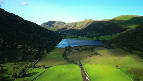 Sunlit-pools-moving-across-lush-green-patchwork-fields-on-valley-floor-with-wooded-mountainsides-and-distant-lake-Brotherswater-on-summer-day