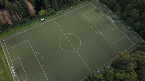 Aerial-Tilt-Down-over-an-idyllic,-empty,-green-Football-Field-with-goals-and-forest-around,-Drone-Footage