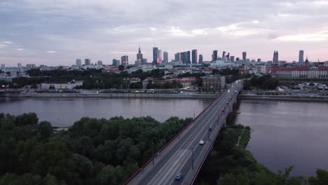 Filmische-Drohnenaufnahmen-Der-Warschauer-Skyline-Mit-Der-Weichsel-Und-Einer-Mit-Verkehr-Gefüllten-Brücke,-Links-Parallaxe-Mit-Wolken