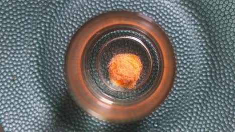 High-angle-view-of-an-orange-effervescent-tablet-dissolving-at-the-bottom-of-a-glass-of-water