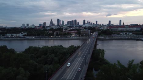 Cinematic-drone-footage-of-Warsaw-skyline-with-vistula-river-and-bridge-filled-with-traffic-in-the-evening