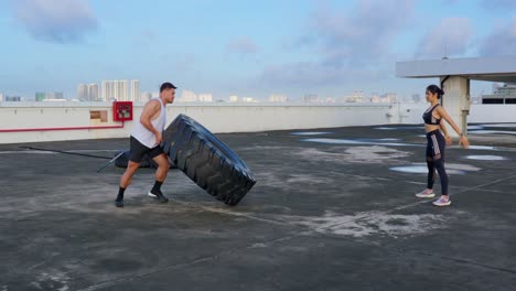 Couple-doing-the-tire-flip-and-squat-exercise-on-the-beautiful-rooftop