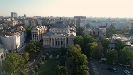 A-Majestic-Aerial-View-of-the-Romanian-Athenaeum-in-Bucharest,-Romania,-with-the-City’s-Skyline-in-the-Background