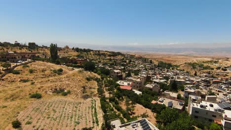 Luftüberflug-über-Die-Libanesische-Stadt,-Umgeben-Von-Wüste-An-Sonnigen-Tagen-Und-Blauem-Himmel---Hügelige-Landschaft-Mit-Häusern-Und-Pflanzen