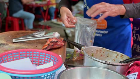 Local-hawker-packing-the-costumer's-orders-of-spicy-minced-meat-called-Laab-and-some-grilled-pork-in-a-bag-in-a-local-restaurant-in-the-streets-of-Bangkok,-Thailand