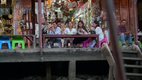 Some-local-tourists-having-a-good-time-with-their-friends-while-eating-and-drinking-in-front-of-the-canal-of-Amphawa-Floating-Market-in-Samut-Songkhram,-Thailand