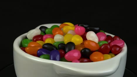 White-bowl-of-colorful-Jelly-beans-rotates-on-black-background