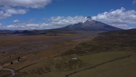 Capture-the-grandeur-of-Cotopaxi-Volcano-in-4K-drone-footage,-as-our-camera-smoothly-pans-across-the-majestic-peak-on-a-sunny-day,-framed-by-the-blue-sky-and-adorned-with-gentle-cloud-veils