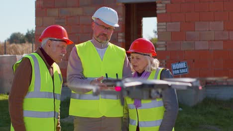 Specialist-worker-fly-on-drone-on-building-construction-site,-showing-house-to-grandparents-clients