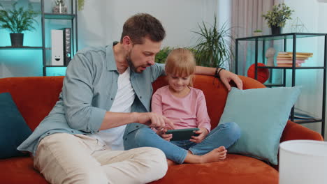 Child-kid-daughter-having-fun-with-father-or-nanny-enjoying-using-smartphone-play-online-games