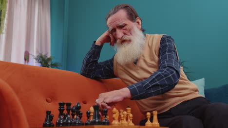 Focused-senior-grandfather-man-playing-chess-leisure-board-game-alone,-domestic-activity-at-home
