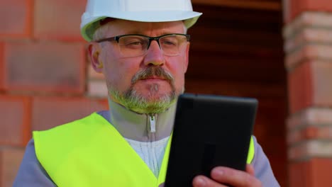 Architect-man-with-digital-tablet-computer-at-construction-site,-analyzing-blueprints-building-house