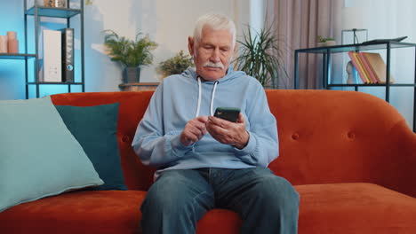 Senior-old-grandfather-sitting-on-sofa,-using-smartphone-share-messages-on-social-media-application
