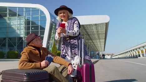Turistas-Jubilados-Mayores-Abuela-Abuelo-Comprar-Boletos-En-Línea-En-El-Teléfono-Móvil-Cerca-Del-Aeropuerto