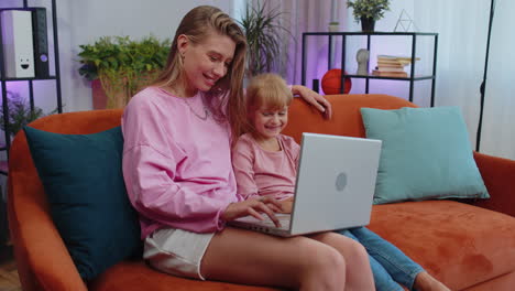 Child-kid-daughter-having-fun-with-mother-or-nanny-enjoying-using-laptop-pc-watch-cartoons-at-home