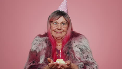 Happy-senior-old-woman-celebrating-birthday-anniversary-party-blowing-candle-on-cake,-making-a-wish