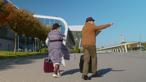 Joyful-grandmother-grandfather-walking-with-luggage-suitcase-bags-to-airport-hall,-celebrate-dancing