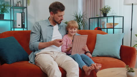 Child-kid-daughter-having-fun-with-father-or-nanny-enjoying-using-digital-tablet-play-game-at-home