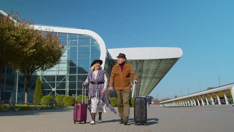 Stilvolles-Familienpaar-Im-Ruhestand,-Oma,-Großvater,-Der-Mit-Gepäckkoffern-Zur-Flughafenhalle-Geht