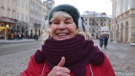 Stylish-old-senior-woman-tourist-smiling,-showing-thumb-up-in-winter-city-center-of-Lviv,-Ukraine