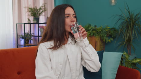 Thirsty-one-young-woman-sitting-at-home-holding-glass-of-natural-aqua-make-sips-drinking-still-water